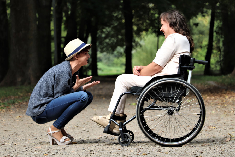 zdjęcie przedstawia osobę kucającą przed drugą osobą siedzącą na wózku inwalidzkim
